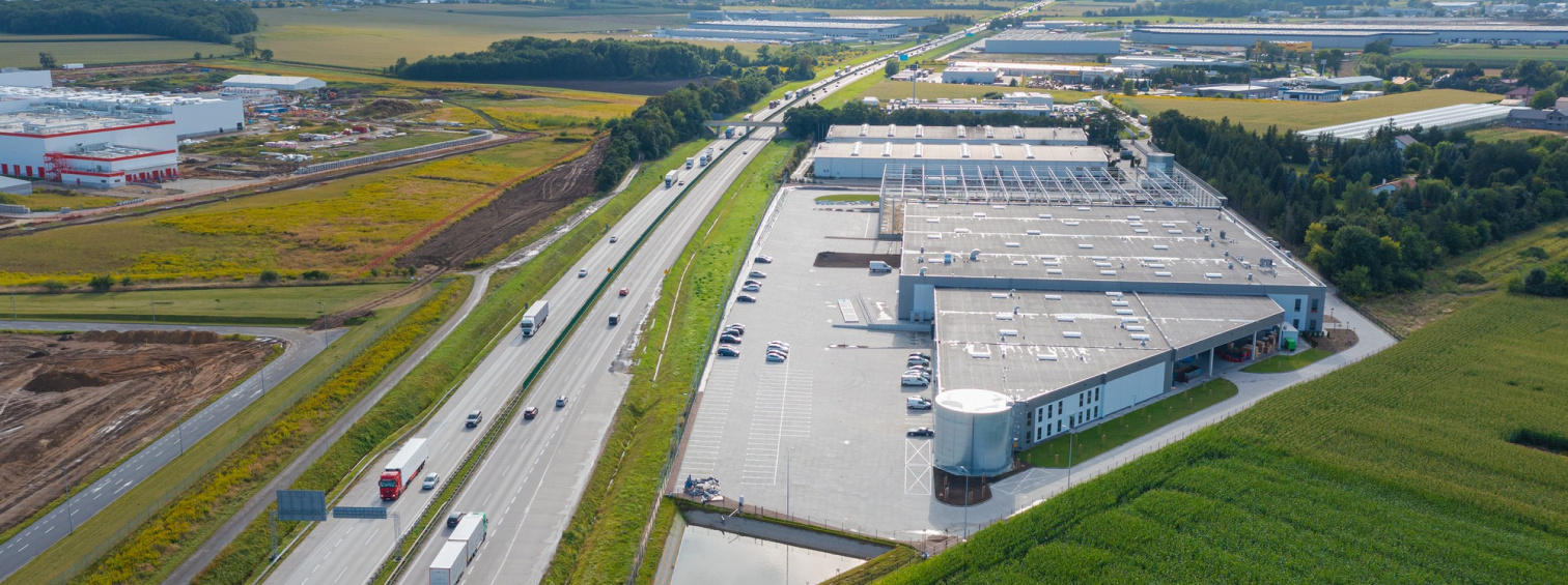 Aerial view of warehouses and loading yards beside a road and green fields.