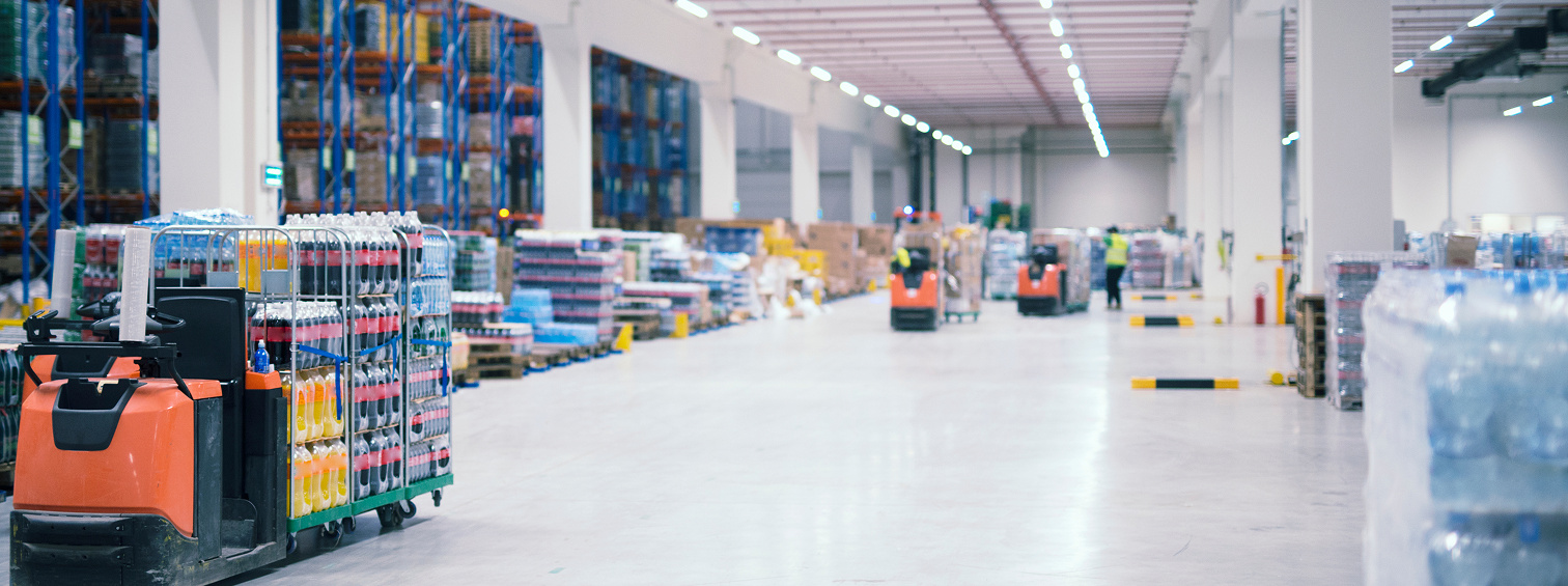 Warehouse interior with forklifts, storage racks and goods along a wide aisle.