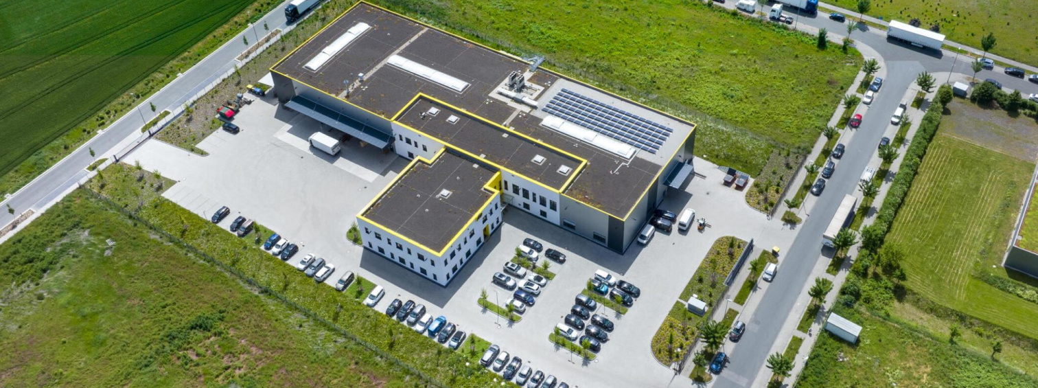 Aerial view of a logistics facility with trucks, parked cars and green fields.