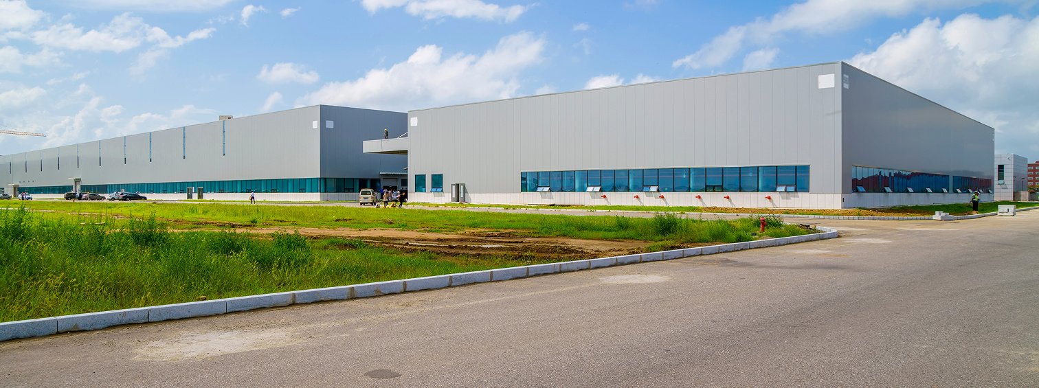 Long warehouse exterior with blue windows beside a paved road.