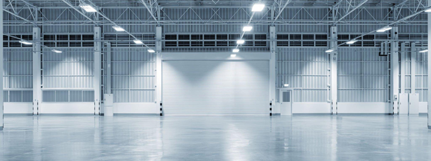 Empty warehouse interior with steel columns, overhead lighting and loading doors.