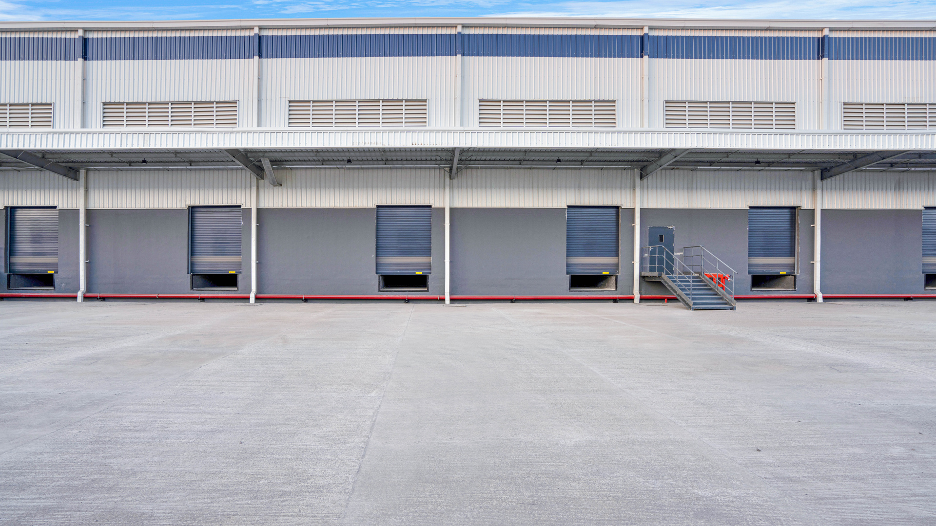 Warehouse exterior with a row of loading dock doors and a paved loading area.
