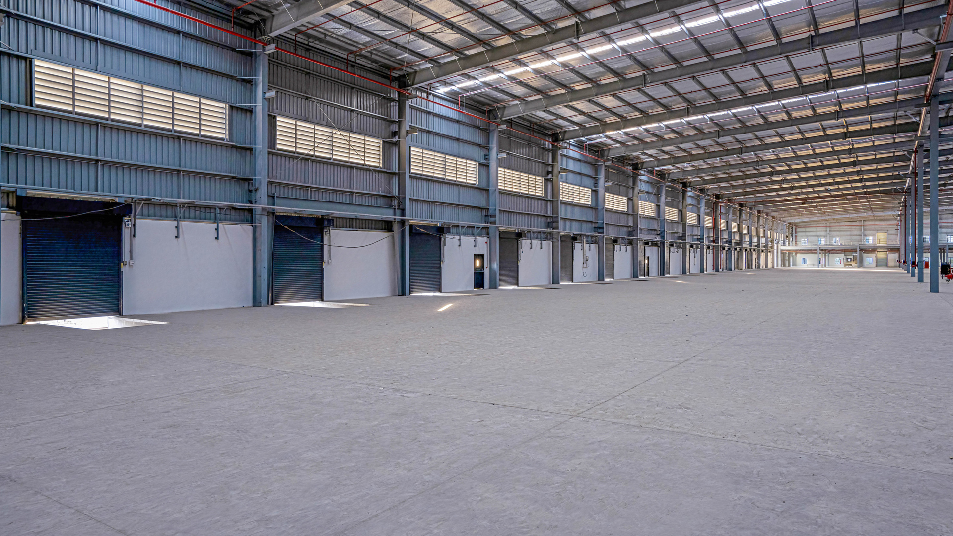 Empty warehouse interior with steel roof trusses and loading doors along one wall.