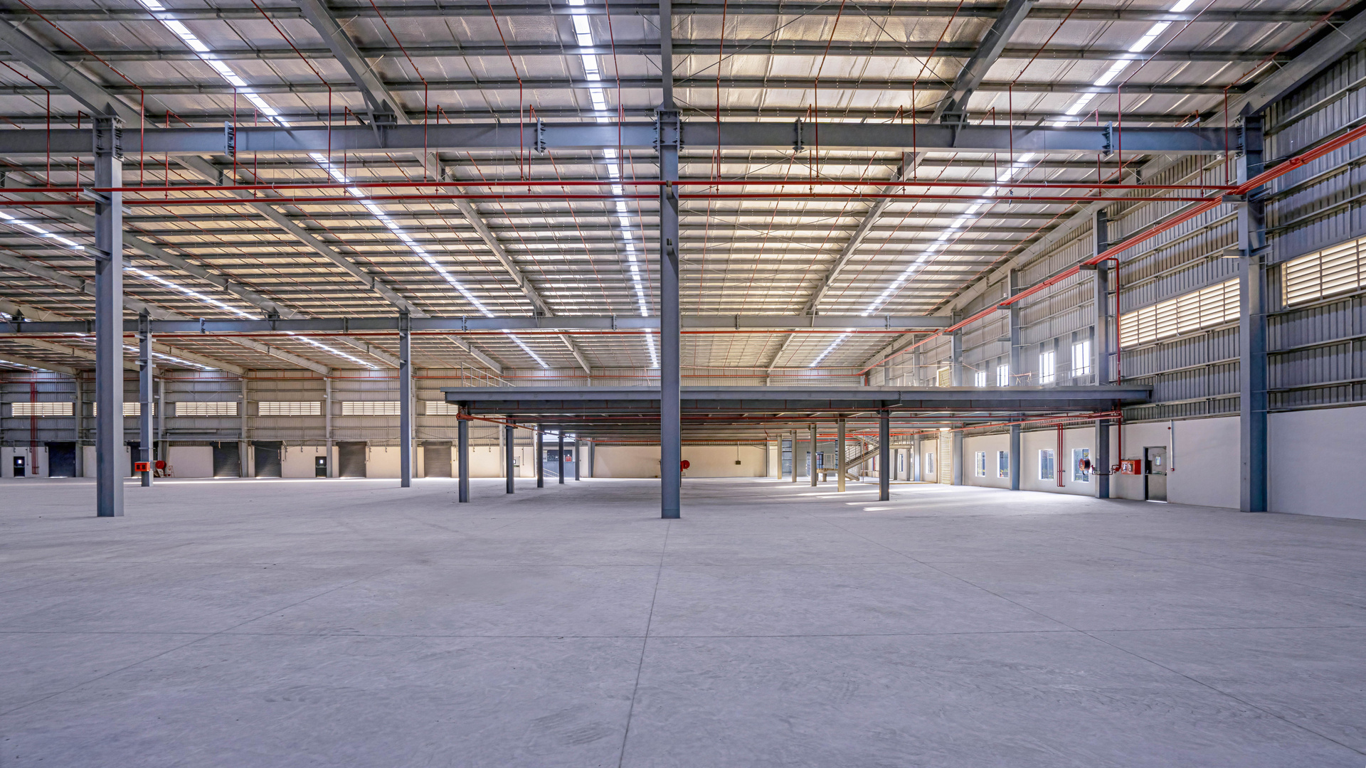 Empty warehouse hall with steel columns, roof lighting and a mezzanine level.