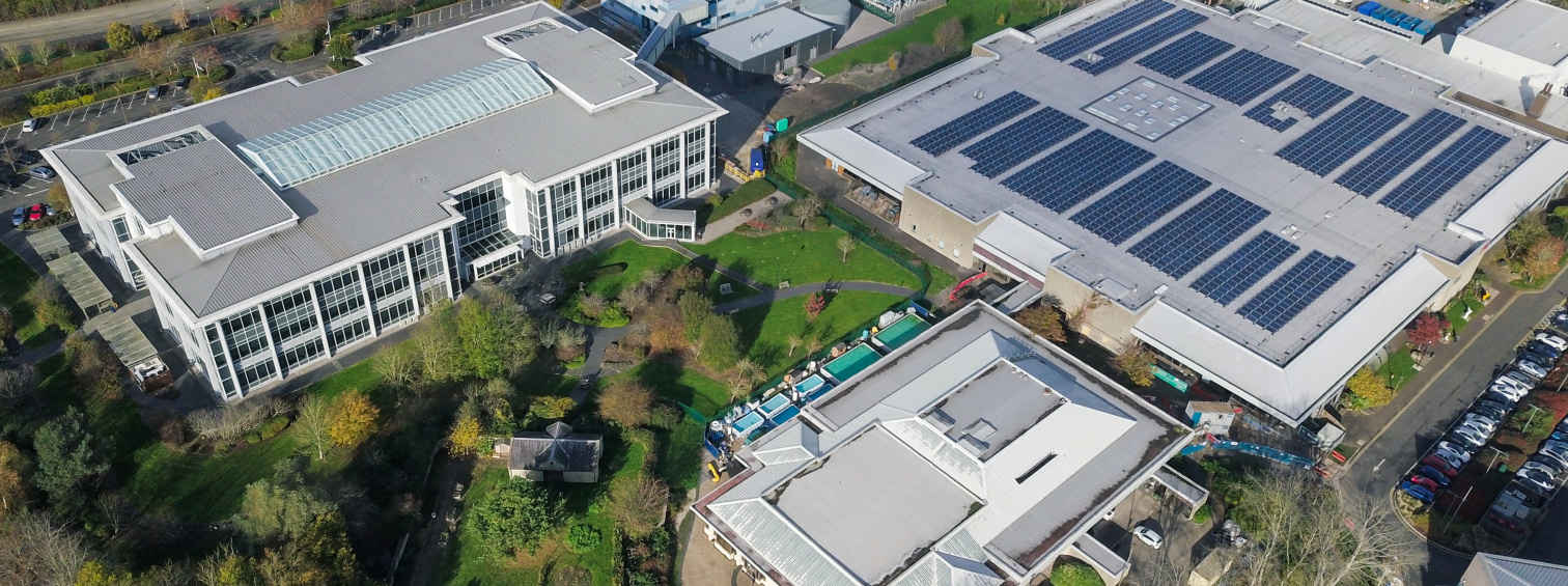 Aerial view of industrial buildings with rooftop solar panels and landscaped grounds.
