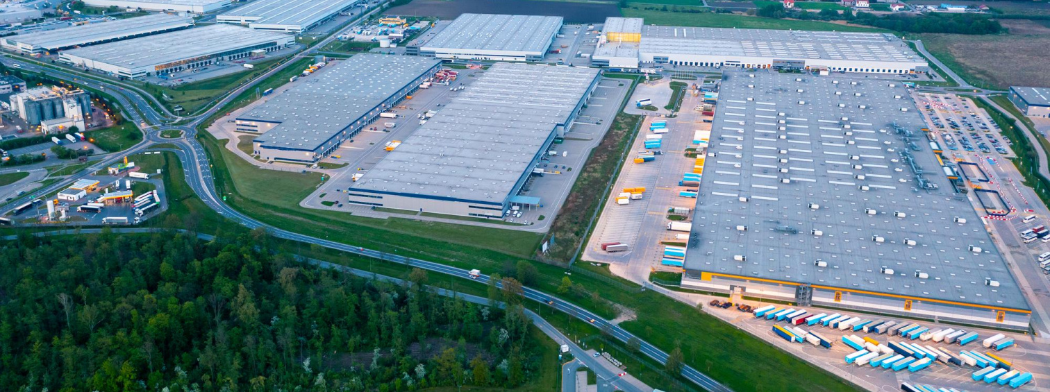 Aerial view of large warehouses with loading yards, trucks and surrounding woodland.