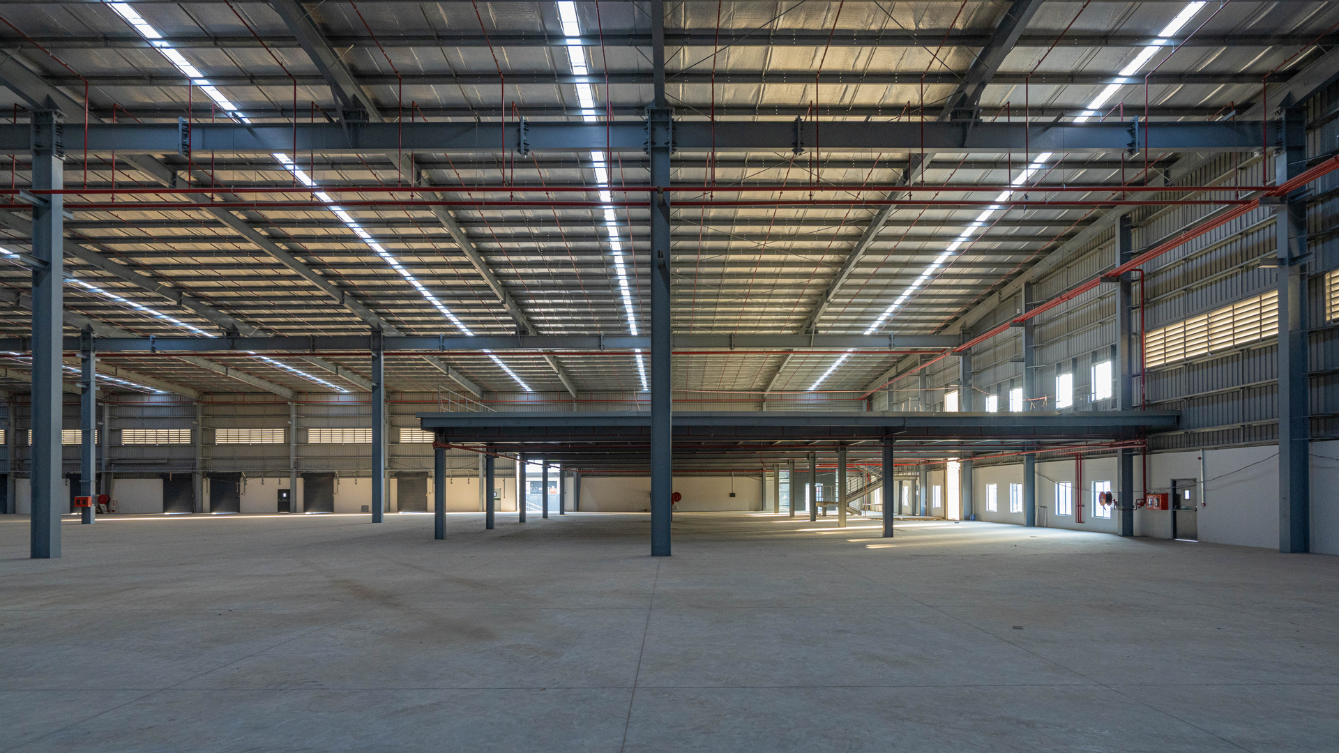 Empty warehouse interior with steel columns, roof lighting and a mezzanine level.