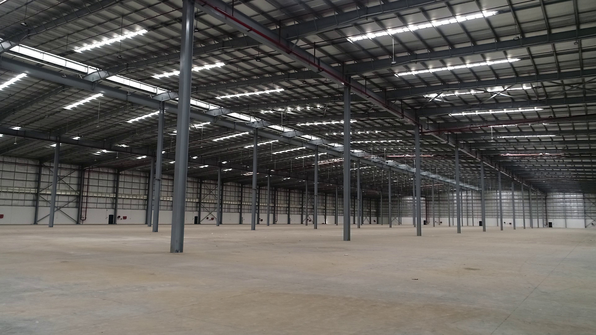 Empty warehouse interior with steel columns, roof lighting and a mezzanine level.